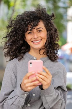 Close-up of Caucasian young woman using smartphone typing text messages in social media application online, surfing internet, relaxing, taking a break outdoors. Lady girl on city street. Vertical