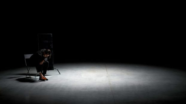 Man in suit cleans his shoes. Stock footage. Theatrical production with one actor in business suit cleaning shoes. Man in suit sits on chair and cleans shoes on stage.