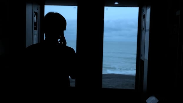 Young tourist with a smartphone looks out of the window of a moving train. Stock clip. Rear view of a male silhouette talking on phone in train