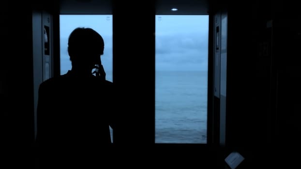 Young man standing next to a train window and looking outside Stock clip. Man with smartphone looking through the window on sea