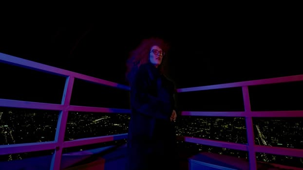 Woman with glasses on roof of building. Media. Fashion woman in coat and glasses stands on roof of high-rise building. Stylish night photo shoot with woman in gloomy image.