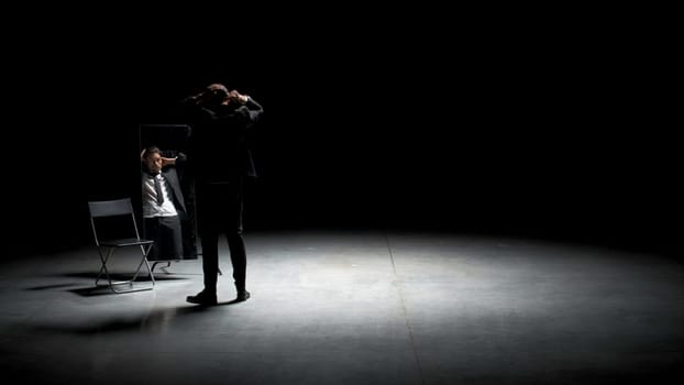 Man combs his hair in front of mirror on stage. Stock footage. Man in suit combs hair in front of mirror. Stage production with one man in suit and mirror.