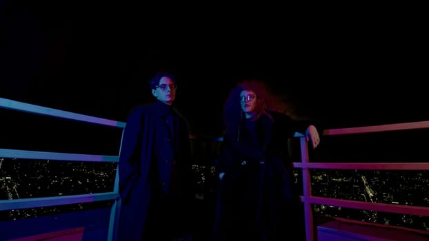 Man and woman on roof at night. Media. Couple of night heroes on roof of high-rise. Man and woman with glasses look like super villains.