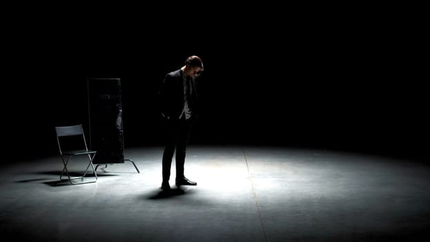 Man in suit alone on theater stage. Stock footage. Single attractive man in suit is playing on stage of theater. Man in suit with mirror is alone on dark theatrical stage.