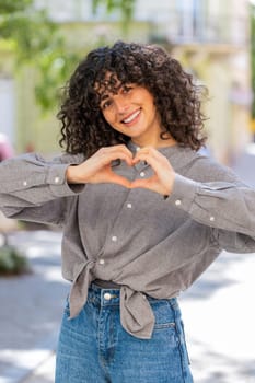 I love you. Caucasian young woman makes symbol of love, showing heart sign to camera express romantic feelings, express sincere positive feelings outdoors. Charity, gratitude, donation. on city street