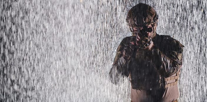 Army soldier in Combat Uniforms with an assault rifle, plate carrier and combat helmet going on a dangerous mission on a rainy night