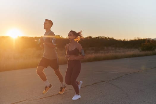 A handsome young couple running together during the early morning hours, with the mesmerizing sunrise casting a warm glow, symbolizing their shared love and vitality.