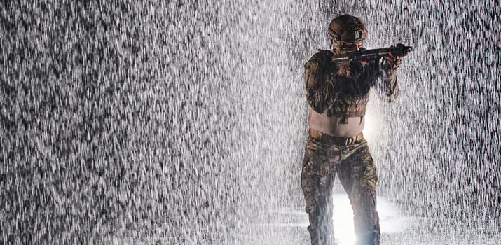 Army soldier in Combat Uniforms with an assault rifle, plate carrier and combat helmet going on a dangerous mission on a rainy night