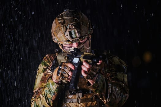 Army soldier in Combat Uniforms with an assault rifle, plate carrier and combat helmet going on a dangerous mission on a rainy night