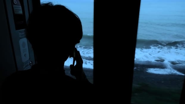 Young man standing next to a train window and looking outside Stock clip. Man with smartphone looking through the window on sea