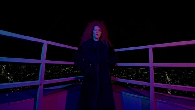 Fashion woman on roof of high-rise. Media. Stylish woman in photo shoot on roof of high-rise at night. Neon photo shoot with woman in coat on high-rise.