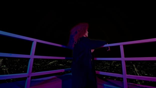 Woman on roof of night city. Media. Stylish fashion shoot with model in coat on roof. Female model in neon night shooting on roof of high-rise.