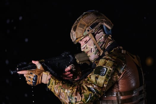 Army soldier in Combat Uniforms with an assault rifle, plate carrier and combat helmet going on a dangerous mission on a rainy night