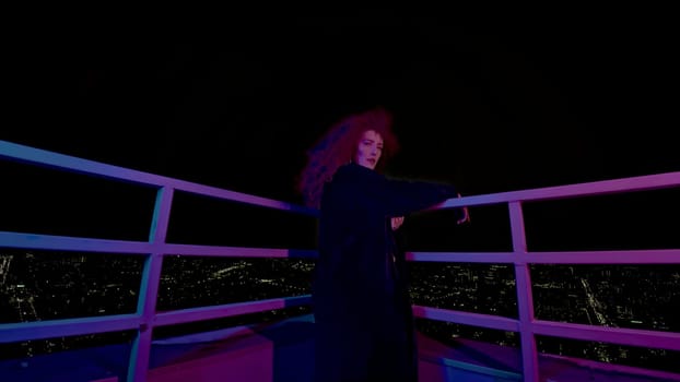 Woman on roof of night city. Media. Stylish fashion shoot with model in coat on roof. Female model in neon night shooting on roof of high-rise.