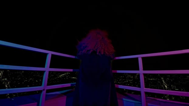 Woman on roof of high-rise building. Media. Modern witch on roof of high-rise at night. Rear view of woman on roof of high-rise at night.
