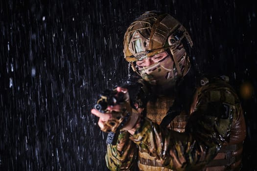 Army soldier in Combat Uniforms with an assault rifle, plate carrier and combat helmet going on a dangerous mission on a rainy night