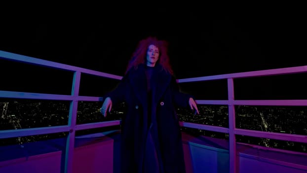 Fashion woman on roof of high-rise. Media. Stylish woman in photo shoot on roof of high-rise at night. Neon photo shoot with woman in coat on high-rise.