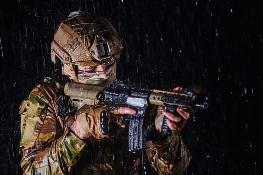 Army soldier in Combat Uniforms with an assault rifle, plate carrier and combat helmet going on a dangerous mission on a rainy night