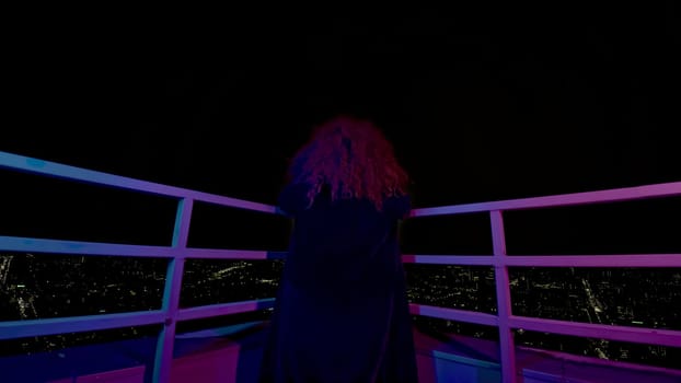 Woman on roof of high-rise building. Media. Modern witch on roof of high-rise at night. Rear view of woman on roof of high-rise at night.