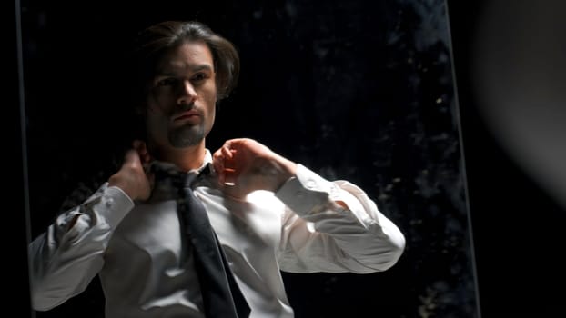 Reflection in mirror of man in suit on black background. Stock footage. Man in suit is preparing for something in front of mirror. Theatrical production with reflection of man in suit in mirror.