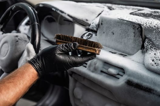 A mechanic cleans the interior of a car with a brush and foam