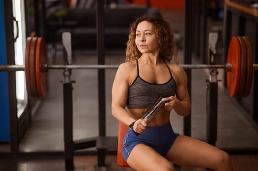 Caucasian forty-year-old woman puts on wrist straps before doing barbell exercises in the gym