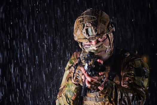 Army soldier in Combat Uniforms with an assault rifle, plate carrier and combat helmet going on a dangerous mission on a rainy night