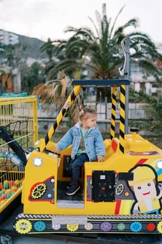 Little girl sits in the cab of a toy tractor, looking back. High quality photo