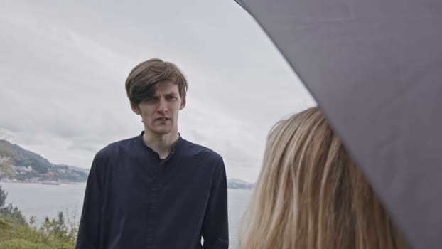 Young couple sharing a day at the beach during cold spring weather. Stock clip. Man and woman with umbrella meeting at the sea shore