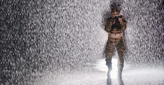 Army soldier in Combat Uniforms with an assault rifle, plate carrier and combat helmet going on a dangerous mission on a rainy night