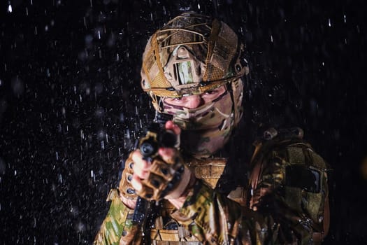 Army soldier in Combat Uniforms with an assault rifle, plate carrier and combat helmet going on a dangerous mission on a rainy night