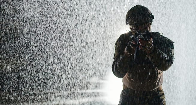 Army soldier in Combat Uniforms with an assault rifle, plate carrier and combat helmet going on a dangerous mission on a rainy night