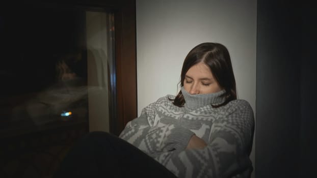 Young woman with anxiety disorder on window. Media. Young woman in sweater is sitting on horse with sad look. Depressed woman falls asleep on window.