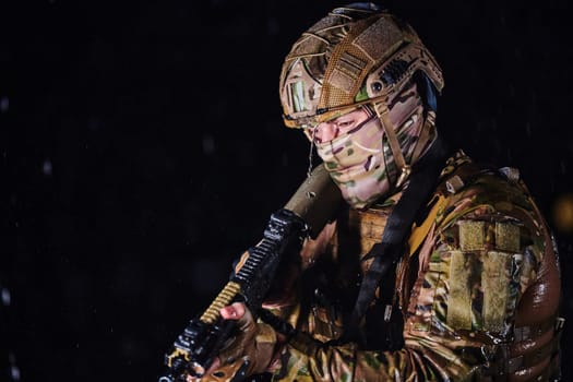 Army soldier in Combat Uniforms with an assault rifle, plate carrier and combat helmet going on a dangerous mission on a rainy night