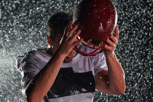 American Football Field: Lonely Athlete Warrior Standing on a Field Holds his Helmet and Ready to Play. Player Preparing to Run, Attack and Score Touchdown. Rainy Night with Dramatic Fog, Blue Light.