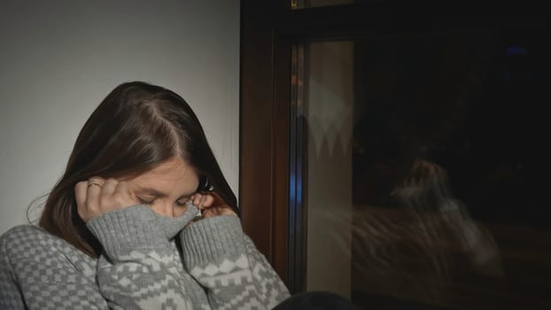 Young woman with depression at window of house. Media. Young woman in sweater is sitting on window. Single woman with depression falls asleep on window of house at night.