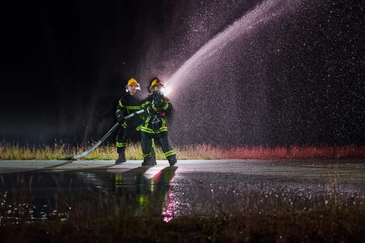 Firefighters using a water hose to eliminate a fire hazard. Team of female and male firemen in dangerous rescue mission