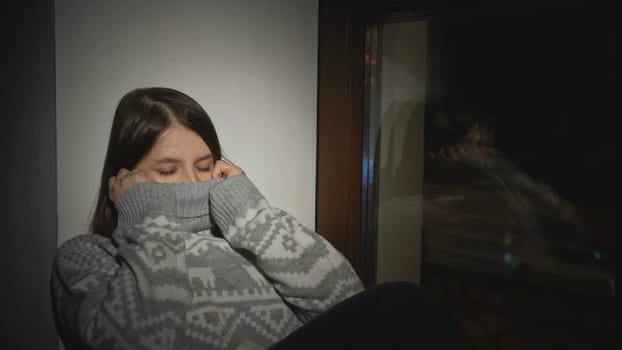 Young woman with anxiety disorder on window. Media. Young woman in sweater is sitting on horse with sad look. Depressed woman falls asleep on window.