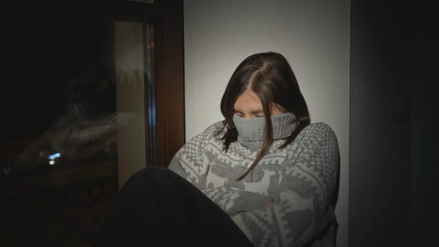 Young woman with depression at window of house. Media. Young woman in sweater is sitting on window. Single woman with depression falls asleep on window of house at night.