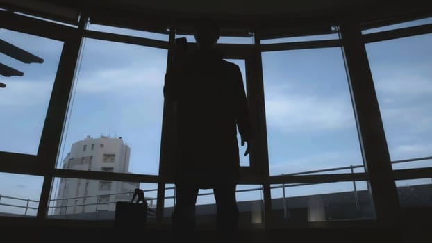 Dark silhouette of man with bag and phone. Stock. View from below of frightening silhouette of man with bag and phone. Dark shadow of man with bag pulls out phone on background of windows.