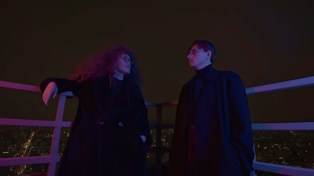 Low angle view of a couple standing on roof and looking at each other. Media. Man and woman with wild beautiful curly hair at night