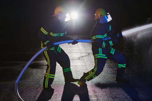 Firefighters using a water hose to eliminate a fire hazard. Team of female and male firemen in dangerous rescue mission