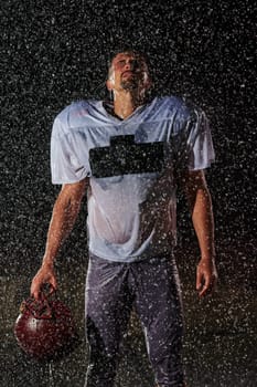 American Football Field: Lonely Athlete Warrior Standing on a Field Holds his Helmet and Ready to Play. Player Preparing to Run, Attack and Score Touchdown. Rainy Night with Dramatic Fog, Blue Light.