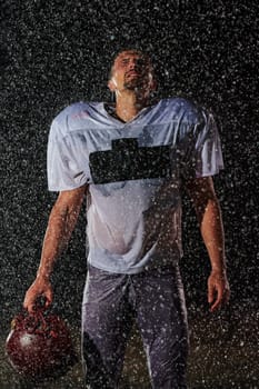 American Football Field: Lonely Athlete Warrior Standing on a Field Holds his Helmet and Ready to Play. Player Preparing to Run, Attack and Score Touchdown. Rainy Night with Dramatic Fog, Blue Light.