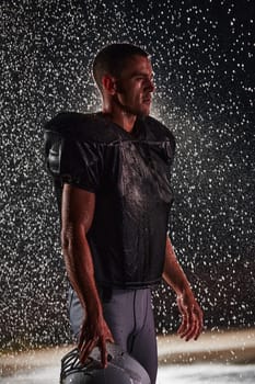 American Football Field: Lonely Athlete Warrior Standing on a Field Holds his Helmet and Ready to Play. Player Preparing to Run, Attack and Score Touchdown. Rainy Night with Dramatic Fog, Blue Light.