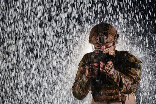 Army soldier in Combat Uniforms with an assault rifle, plate carrier and combat helmet going on a dangerous mission on a rainy night