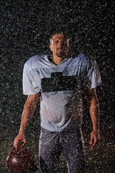 American Football Field: Lonely Athlete Warrior Standing on a Field Holds his Helmet and Ready to Play. Player Preparing to Run, Attack and Score Touchdown. Rainy Night with Dramatic Fog, Blue Light.