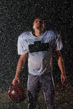 American Football Field: Lonely Athlete Warrior Standing on a Field Holds his Helmet and Ready to Play. Player Preparing to Run, Attack and Score Touchdown. Rainy Night with Dramatic Fog, Blue Light.