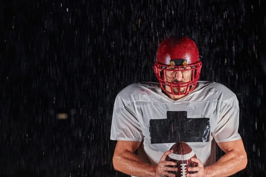 American Football Field: Lonely Athlete Warrior Standing on a Field Holds his Helmet and Ready to Play. Player Preparing to Run, Attack and Score Touchdown. Rainy Night with Dramatic Fog, Blue Light.