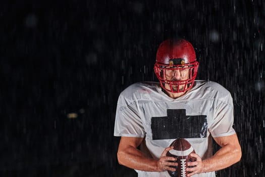 American Football Field: Lonely Athlete Warrior Standing on a Field Holds his Helmet and Ready to Play. Player Preparing to Run, Attack and Score Touchdown. Rainy Night with Dramatic Fog, Blue Light.